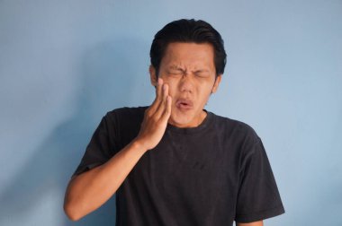 Diş ağrısı ifadesi olan siyah tişörtlü Asyalı genç bir adam. Beyaz arkaplanda izole.