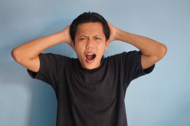 Beyaz arka planda siyah tişörtlü Asyalı genç adamın şaşırmış ifadesi..