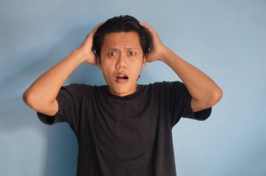 Beyaz arka planda siyah tişörtlü Asyalı genç adamın şaşırmış ifadesi..