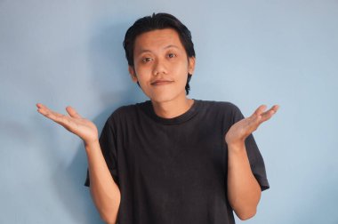 Siyah tişört giyen yakışıklı Asyalı adam elini kaldırırken ayakta ve mutlu görünüyor.