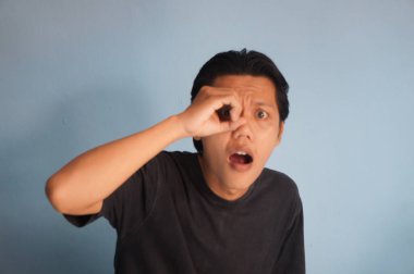 Siyah tişört giyen yakışıklı Asyalı genç adam şaşırmış yüz ifadesiyle şaşırmış ve parmaklarından içeri bakıyor. İnançsız ifade.