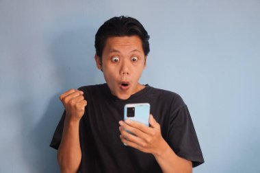 Elinde akıllı telefon tutarken siyah tişört giyen heyecanlı Asyalı genç adam