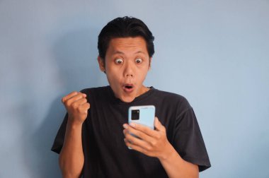 Elinde akıllı telefon tutarken siyah tişört giyen heyecanlı Asyalı genç adam