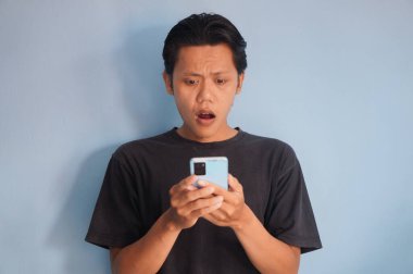 Siyah tişört giyen genç Asyalı adam akıllı telefona bakarken şaşırdı.