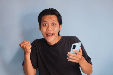 Elinde akıllı telefon tutarken siyah tişört giyen heyecanlı Asyalı genç adam