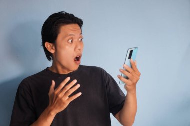 Siyah tişört giyen genç Asyalı adam akıllı telefona bakarken şaşırdı.