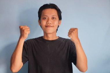 Mutlu Asyalı genç adam başarıyı ya da başarıyı kutlamak için kolunu kaldırıyor.