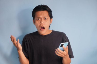 Genç Asyalı adam cep telefonu tutarken kafası karışık bir yüz ifadesi sergiliyor