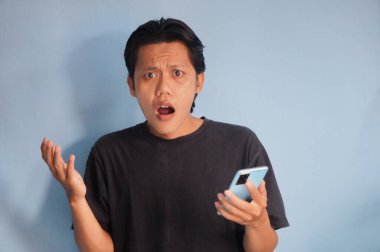 Genç Asyalı adam cep telefonu tutarken kafası karışık bir yüz ifadesi sergiliyor