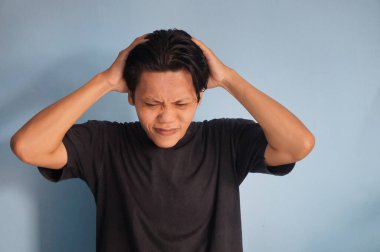 Asyalı genç bir adam stres hareketi göstererek başını tutuyor..