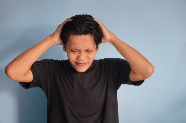 Asyalı genç bir adam stres hareketi göstererek başını tutuyor..