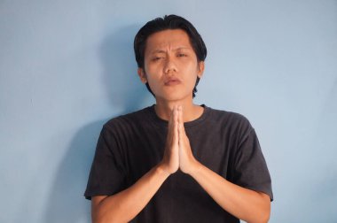 Siyah tişört giyen yakışıklı Asyalı genç adam ellerinin birbiri ile dua ederek af diliyor.