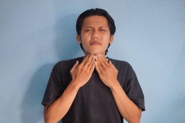 Siyah tişört giyen Asyalı genç adam boğaz ağrısı çekiyor. 