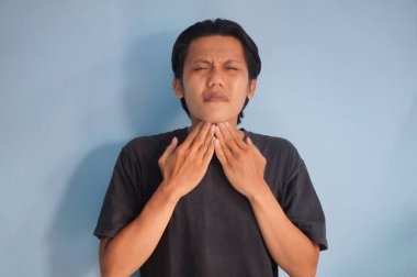 Siyah tişört giyen Asyalı genç adam boğaz ağrısı çekiyor. 