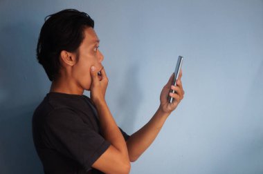 Siyah tişört giyen genç Asyalı adam akıllı telefona bakarken şaşırdı.