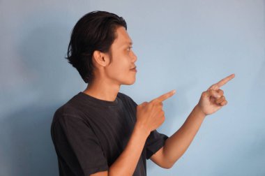 Siyah tişörtlü yakışıklı Asyalı adam parmağını boş bir yere doğrultuyor. gösterme seçeneği, öneri, sunum