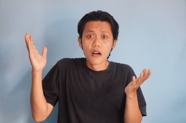 Siyah tişört giyen genç Asyalı adam, kafası karışık bir yüz ifadesi sergiliyor.