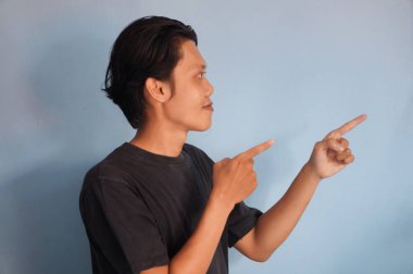 Siyah tişörtlü yakışıklı Asyalı adam parmağını boş bir yere doğrultuyor. gösterme seçeneği, öneri, sunum