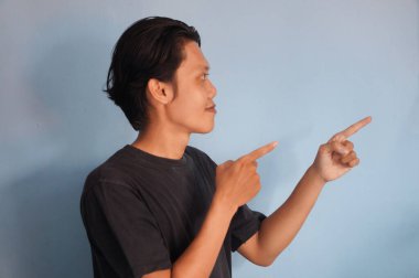 Siyah tişörtlü yakışıklı Asyalı adam parmağını boş bir yere doğrultuyor. gösterme seçeneği, öneri, sunum