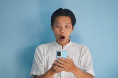 Beyaz tişörtlü genç Asyalı adam akıllı telefona bakarken şaşırdı.