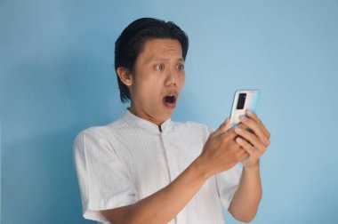 Beyaz tişörtlü genç Asyalı adam akıllı telefona bakarken şaşırdı.