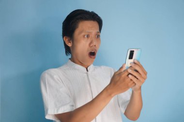 Beyaz tişörtlü genç Asyalı adam akıllı telefona bakarken şaşırdı.