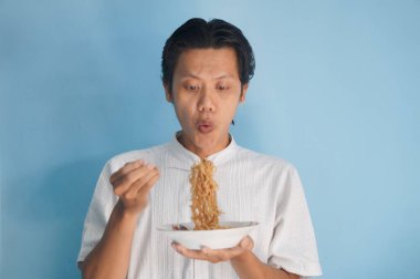 Erişte yemekten hoşlanan Asyalı genç bir adamın portresi. Öğle yemeği konsepti.