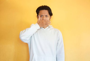 Kapüşonlu ciddi bir Asyalı gencin resmi sessizlik işareti gösteriyor ve sır saklayacağına söz veriyor.