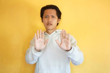 Kapüşonlu yakışıklı Asyalı genç adam dur hareketi yapıyor..