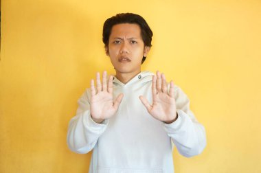 Kapüşonlu yakışıklı Asyalı genç adam dur hareketi yapıyor..