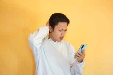 Asyalı genç adam cep telefonu tutarken şaşkın yüz ifadesi gösteriyor.