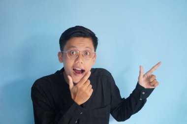 Gözlüklü, siyah gömlekli neşeli Asyalı genç adam yan tarafı işaret ediyor.