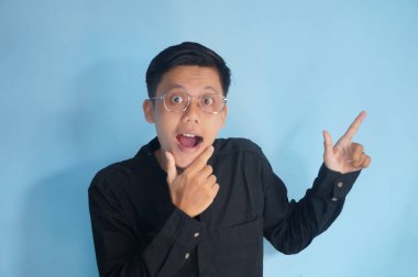 Gözlüklü, siyah gömlekli neşeli Asyalı genç adam yan tarafı işaret ediyor.