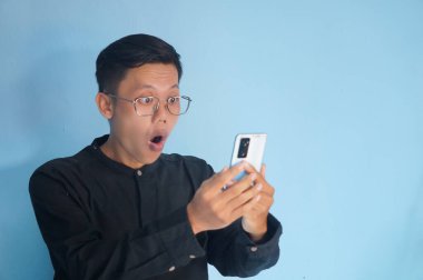 Asyalı genç adam telefonuna şaşkın bir ifadeyle bakıyor.