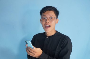 Genç Asyalı adam cep telefonu tutarken mutlu bir yüz ifadesi gösteriyor.