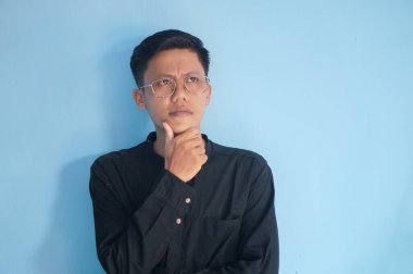 Siyah tişörtlü Asyalı genç bir adam bir şey düşünüyor..