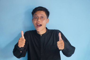 Asyalı genç adam gülümsüyor ve baş parmağını bırakıyor.