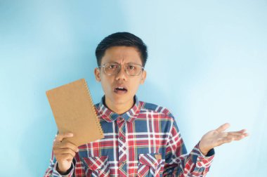 Genç Asyalı bir adam kafası karışmış bir kitap tutuyor.