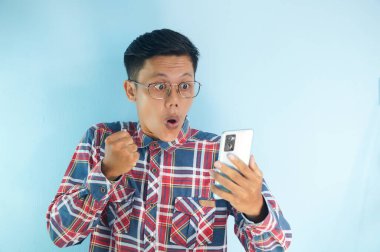 Asyalı genç adam telefonuna şaşkın bir ifadeyle bakıyor.