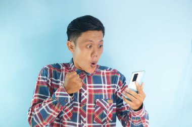 Asyalı genç adam telefonuna şaşkın bir ifadeyle bakıyor.