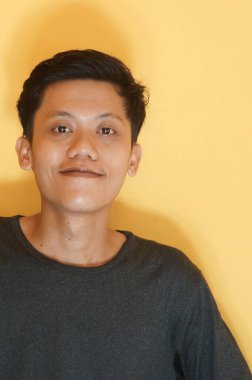 Kameraya bakarken siyah tişört giyen gülümseyen Asyalı genç adam.