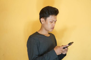 Genç Asyalı adam üzgün bir ifadeyle cep telefonuna bakıyor.