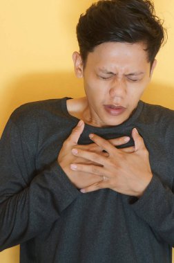 Asyalı genç adam göğüs ağrısı ifadesi olan siyah bir tişört giyiyor.