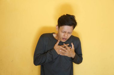 Asyalı genç adam göğüs ağrısı ifadesi olan siyah bir tişört giyiyor.