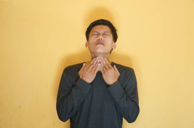 Siyah tişört giyen Asyalı genç adam boğaz ağrısı çekiyor.