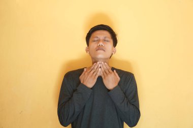 Siyah tişört giyen Asyalı genç adam boğaz ağrısı çekiyor.