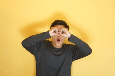 Genç Asyalı adam elleriyle dürbün yapıyor ve şok olmuş bir ifadeyle bakıyor.