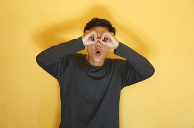 Genç Asyalı adam elleriyle dürbün yapıyor ve şok olmuş bir ifadeyle bakıyor.