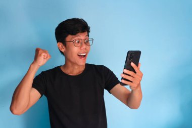 Asyalı genç adam telefonuna şaşkın bir ifadeyle bakıyor.