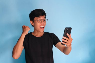 Asyalı genç adam telefonuna şaşkın bir ifadeyle bakıyor.